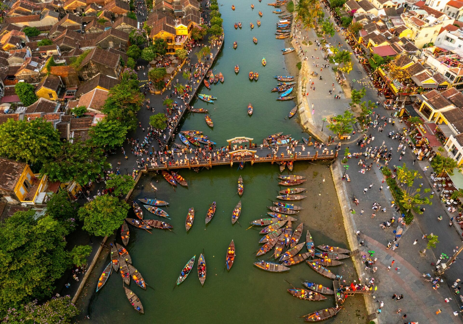 A lively aerial scene with boats, bridge, and colorful town, showcasing a bustling riverside activity.